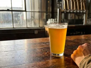 Recepten en Blog 3 Kristalhelder glas goudkleurig tarwebier op rustieke houten bar met natuurlijk licht door brouwerij raam